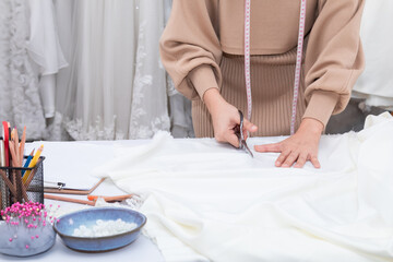 Obraz na płótnie Canvas Selective focus close up of hand working woman cutting fabric with scissors while sewing custom made clothes and design wedding dress in work shop. Fashion designer work at creative office.