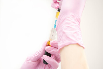 The hands of a doctor cosmetologist in pink gloves hold a test tube with blood plasma and draw it...
