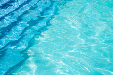 Ladder in the pool and turquoise textured water background. Reflection of the sun in the pool.