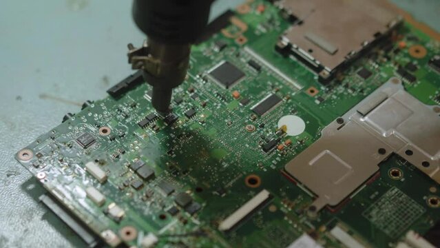 Electronic repair service center worker soldering electic board components with heat gun. Technician warming up microchip to fix computer motherboard.