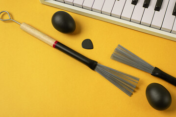 Drum brushes, shakers, midi keyboard and guitar picks on a bright yellow background. Top view, space for text.