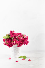 Romance dry pink roses in white basket as bridal bouquet on soft light white table and elegant marble wall, copy space, vertical. Elegant floral background for wedding, anniversary, greeting card.