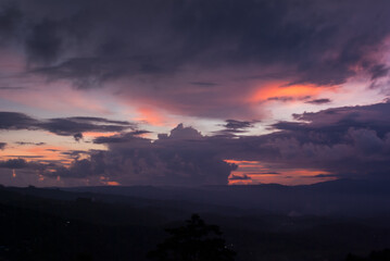 Indonesian colorful dramatic landscape - beautiful sunset with saturated purple, orange, yellow, violet clouds on blue sky in evening over dark hazy valley on Bali, Munduk village.