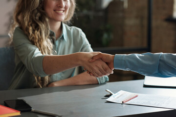 Close-up of happy young woman shaking hand with her employer at table, she getting a job after...