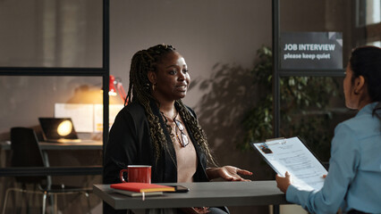 Young African woman presenting her resume to employer at table during job interview at office