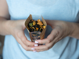 In female hands is a paper bag with dry herbal tea