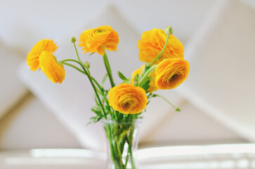 Bouquet of yellow flowers, ranunculus in a vase on a table in a cozy home on a sunny day in bedroom