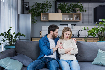 Fototapeta premium A man tries to support and calm a sad woman, a married couple sitting on a sofa at home