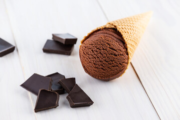 Brown ice cream in a waffle cone with chocolate on a wooden table.