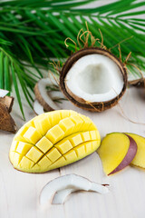 Sliced ​​ripe mango with coconut and palm branch on a wooden background.
