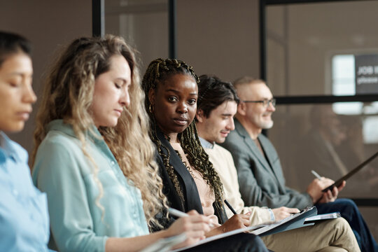 Portrait of African young woman looking at camera while filling application among candidates for job interview