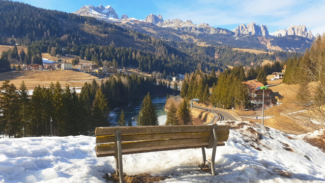 Lonely bench overlooking the mountain landscape of the city of Moena. Panorama.