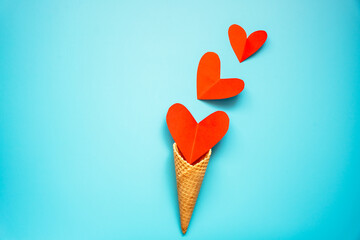 Eine Eiswaffel Tüte gefüllt mit kleinen roten Papier Herzen auf einem blauen Hintergrund. Liebe.
