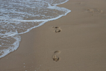 Footprints in the sand beach. Footprints in the sand against a sea wave. Footprints on a sunny day with golden sand, beach, wave and footsteps