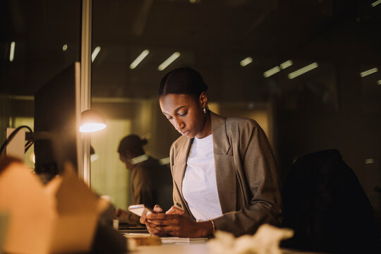 Businesswoman text messaging on smart phone while working in office at night