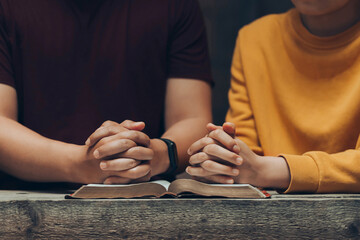 young couples hands folded praying over a Bible. praying with his hands together over a closed Bible, Holy Bible in church concept for faith, spirituality, worship, and religion.