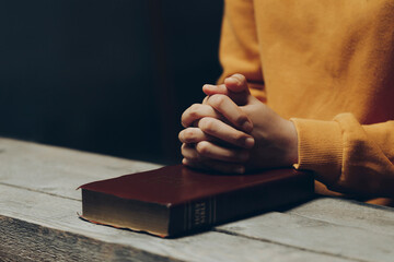 Hands of praying young woman and Bible on a wooden table. Pray for god blessing to wishing have a...