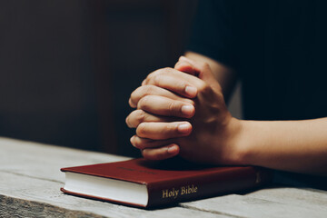 Hands of praying young man and Bible on a wooden table. Pray for god blessing to wishing have a...