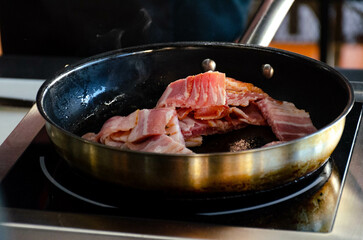 frying pan on a small stove with pieces of smoked bacon