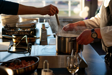 in the restaurant kitchen, the chef's hands hold a saucepan over the stove, a woman's hand stirs the dish with a whisk, together they cook a delicious dish