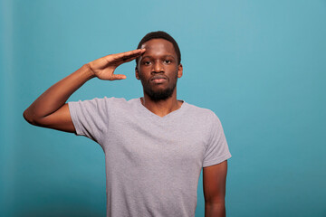 Young man doing military salute with hand over forehead, advertising honor and trustworthy respect...