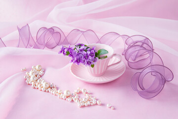 ピンクのコーヒーカップのスミレの花束と真珠