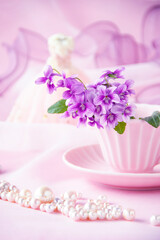 Obraz na płótnie Canvas ピンクのコーヒーカップのスミレの花束と真珠