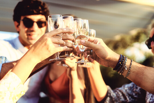 Trendy friends drinking and toasting at rooftop party - group of young people having fun together at patio - friendship lifestyle concept with bright filters - focus on glasses