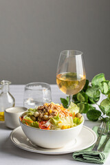 Restaurant table setting with classic tuna salad bowl with different lettuce and vegetables served with white wine glass, water and cutlery.