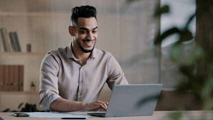 Smiling happy arab man worker businessman finished task computer work relax sit at workplace desk put hands behind head feel satisfied with work well done stress relief taking break after success deal