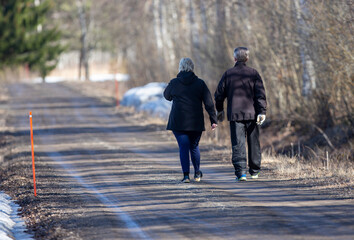 Unidentified caucasian elderly couple walking on the road and enjoying the beautiful nature.