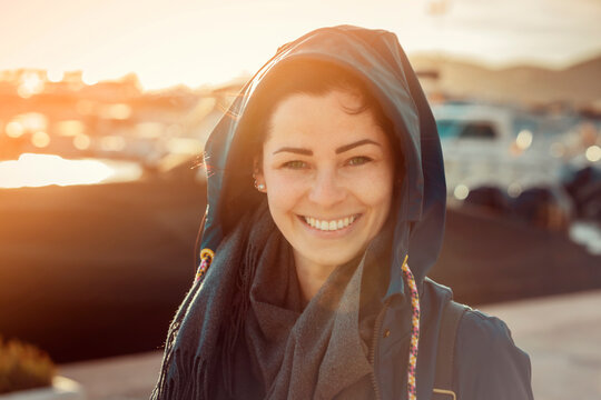 Young woman with rain coat in Ibiza city port at sunset, smiling into the camera