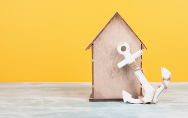 Wooden house with an anchor, yellow background, buying or renting a house, real estate concept,...