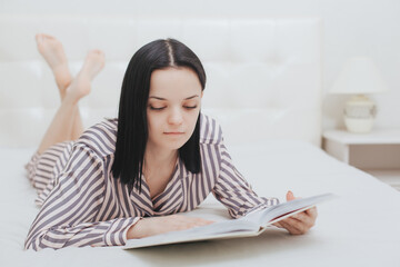 Naklejka premium Barefoot young teenage girl lying on her bed reading a book or studying