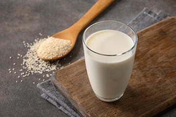 Sesame milk and spoon with sesame seeds on brown background. Close up. Space for text. Lack of...