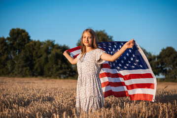 Portrait of a beautiful smiling girl with flag of USA in the field of rye. Patriotic girl with flag of United States