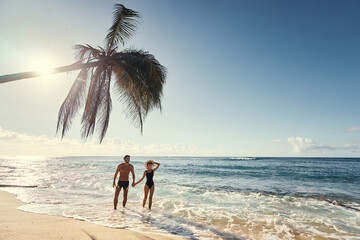Honey moon on the sea shore. Back view of loving couple walking together on beautiful tropical white sand beach.
