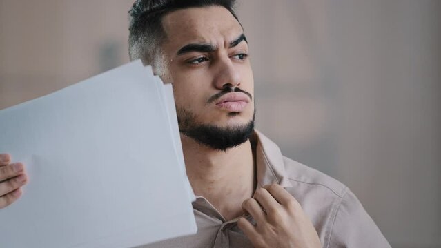 Overheated man hispanic businessman employee suffer from heat high temperature problem at office workplace without air conditioner annoyed male worker feeling hot uncomfortable waving papers cooling