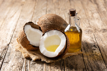 sliced coconuts with oil inside and bottle of coconut oil on wooden table