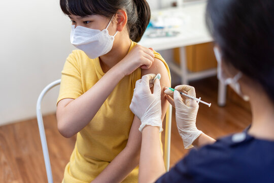 Asian Preteen Girl Getting Vaccinated, Receiving Coronavirus Vaccine Injection in clinic.