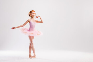 Little ballerina dancer in a pink tutu academy student posing on a white background