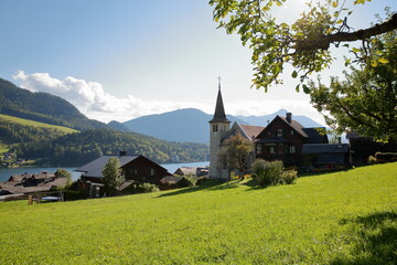 Fototapeta na wymiar Grundlsee village overlooking Grundlsee lake (Western part) with the Catholic church (Pfarrkirche Herz Jesu) in the foreground, Salzkammergut, Styria, Austria, Europe