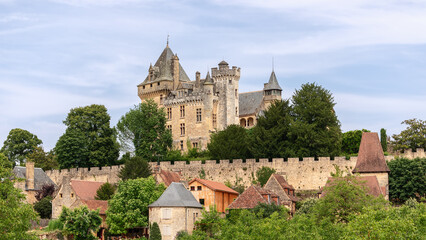 Fototapeta na wymiar Chateau de Montfort on hill top and village huddled below substantial ramparts of castle with attractive houses in Dordogne region, France