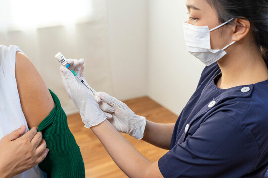 Elderly Asian woman getting coronavirus vaccine by nurse. Medical worker prepare syringe.