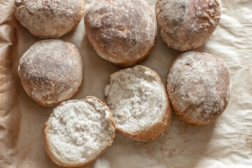 Fresh baked wheat-rye buns with one cracked in half on baking paper.