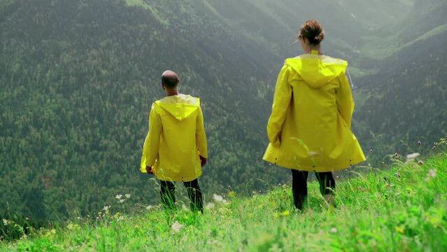 A young woman in a yellow raincoat goes down the slope to a man and covers his eyes with her hands, a young couple rejoices at each other. Travel and tourism