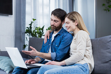Married couple man and woman sitting together at home on the couch using laptop for video chat and chatting with friends