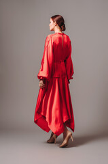 Bright young lady in red oversize dress with long wide sleeves and sexy neckline on high heels...