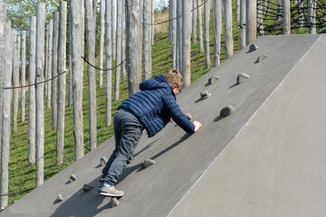 Boy climbs a wall in a children's play park in nature