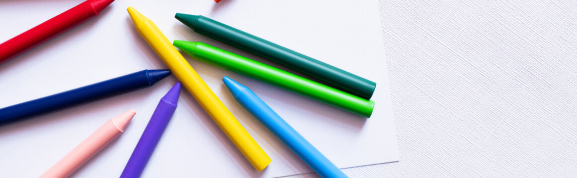 top view of colorful crayons on white paper and textured background, banner.